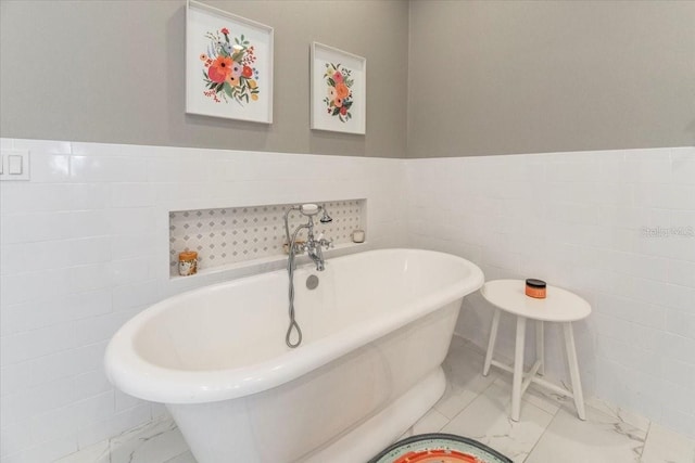 full bathroom featuring marble finish floor, wainscoting, tile walls, and a soaking tub