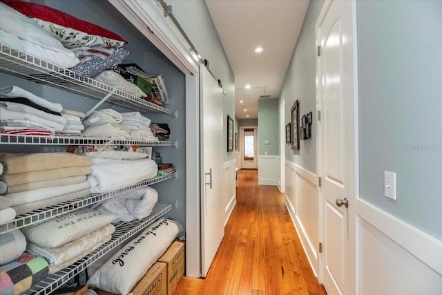 hall with light wood-style floors, a wainscoted wall, and recessed lighting