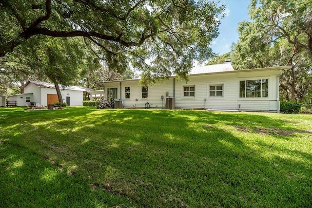 rear view of house with a yard, metal roof, a chimney, and central AC unit
