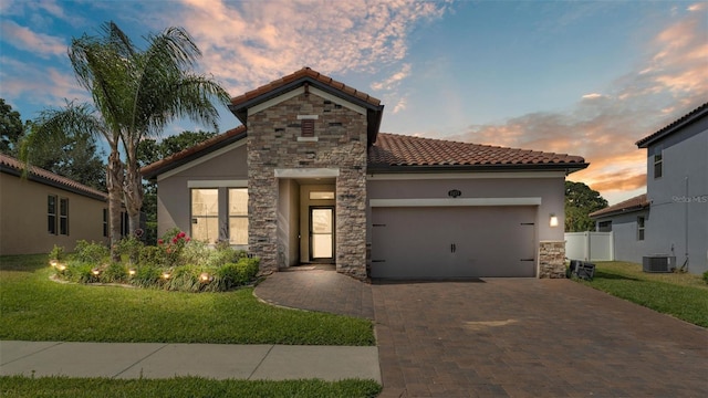 mediterranean / spanish-style home with stone siding, decorative driveway, stucco siding, a tiled roof, and an attached garage