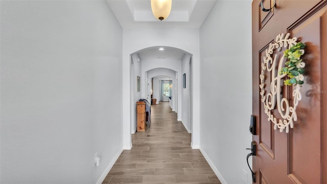 corridor with arched walkways, baseboards, and wood finished floors