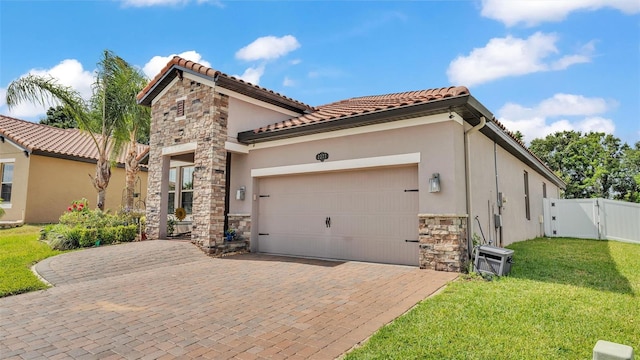 mediterranean / spanish-style home featuring a front yard, a gate, a garage, stone siding, and stucco siding