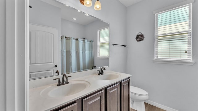 bathroom featuring a sink, baseboards, toilet, and double vanity