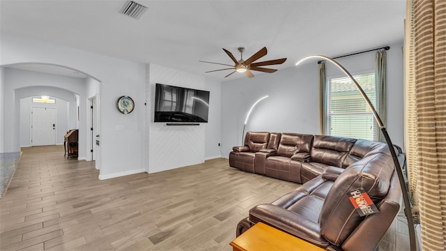 living area featuring a ceiling fan, visible vents, arched walkways, baseboards, and light wood-style floors