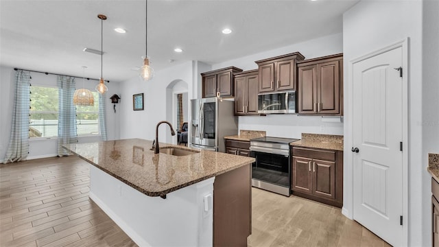kitchen featuring a sink, light wood finished floors, appliances with stainless steel finishes, and arched walkways