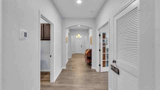 hallway featuring light wood-style floors, arched walkways, baseboards, and recessed lighting