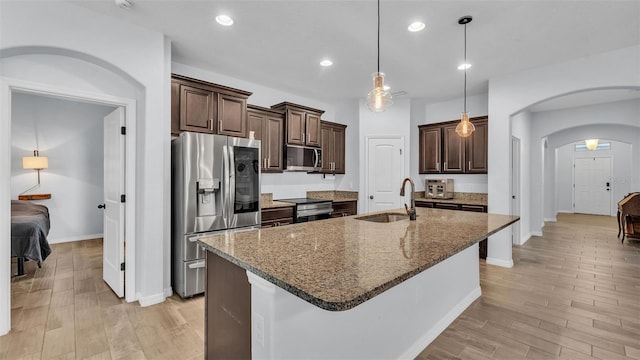 kitchen with appliances with stainless steel finishes, arched walkways, dark brown cabinets, a sink, and light wood-style flooring