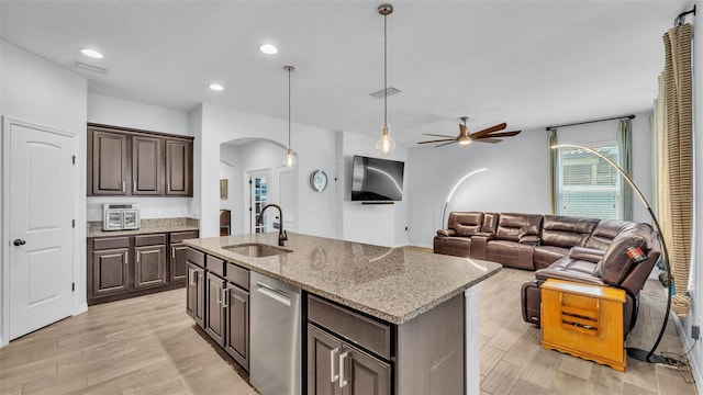 kitchen with ceiling fan, dark brown cabinetry, arched walkways, a sink, and light stone counters