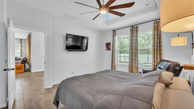 bedroom featuring baseboards, a raised ceiling, ceiling fan, and light wood finished floors