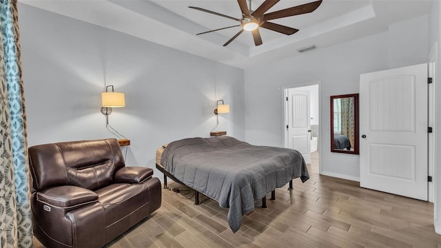 bedroom with visible vents, wood finished floors, baseboards, a raised ceiling, and a ceiling fan