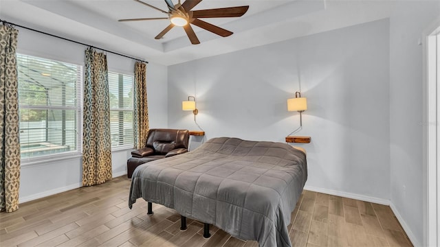 bedroom with a raised ceiling, multiple windows, baseboards, and wood finished floors