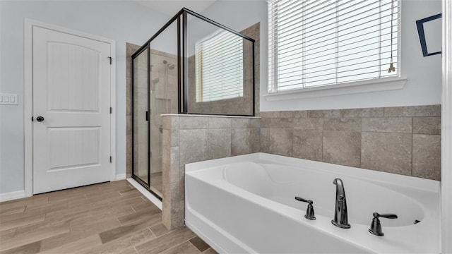 bathroom featuring a shower stall, a healthy amount of sunlight, a bath, and wood finished floors