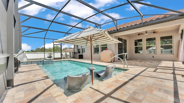 view of pool featuring glass enclosure, a pool with connected hot tub, a ceiling fan, and a patio area