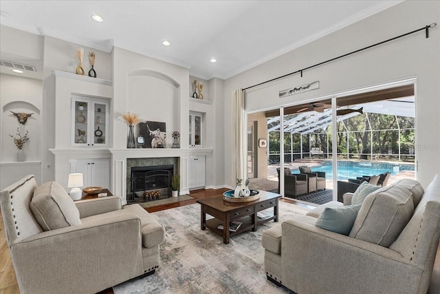 living area with a tiled fireplace, wood finished floors, visible vents, crown molding, and a sunroom