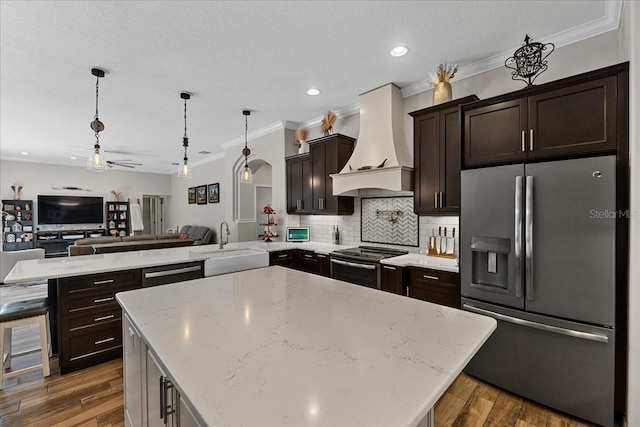 kitchen with stainless steel appliances, custom exhaust hood, a peninsula, a kitchen island, and open floor plan
