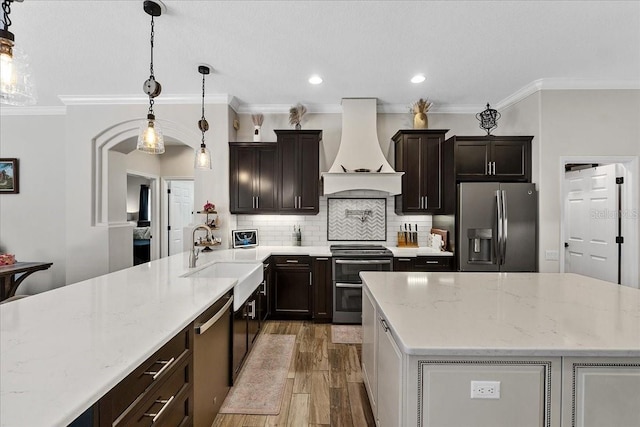 kitchen with custom range hood, a sink, appliances with stainless steel finishes, light wood finished floors, and backsplash