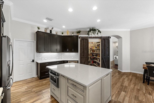 kitchen with light wood finished floors, a center island, stainless steel refrigerator with ice dispenser, backsplash, and arched walkways