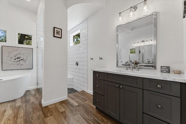 full bathroom with wood finished floors, walk in shower, a freestanding tub, vanity, and baseboards