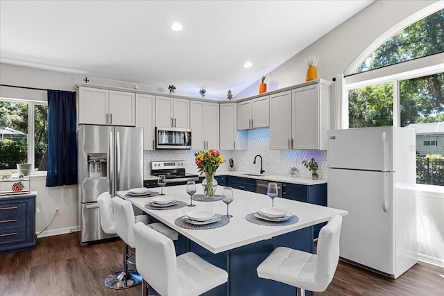 kitchen featuring appliances with stainless steel finishes, light countertops, backsplash, dark wood-style floors, and a kitchen breakfast bar