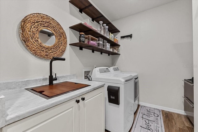 laundry room featuring wood finished floors, washer and dryer, cabinet space, a sink, and baseboards