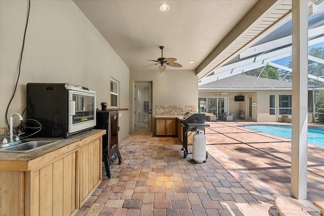 outdoor pool featuring a patio, glass enclosure, an outdoor kitchen, a sink, and a ceiling fan