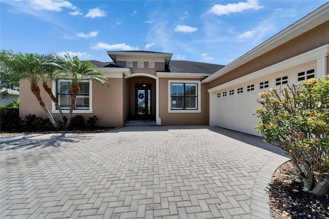 1295 Osprey Landing Dr, Lakeland, FL 33813 - view of exterior entry with stucco siding, decorative driveway, a shingled roof, and an attached garage