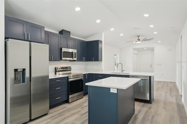 kitchen featuring appliances with stainless steel finishes, a sink, light countertops, a peninsula, and vaulted ceiling