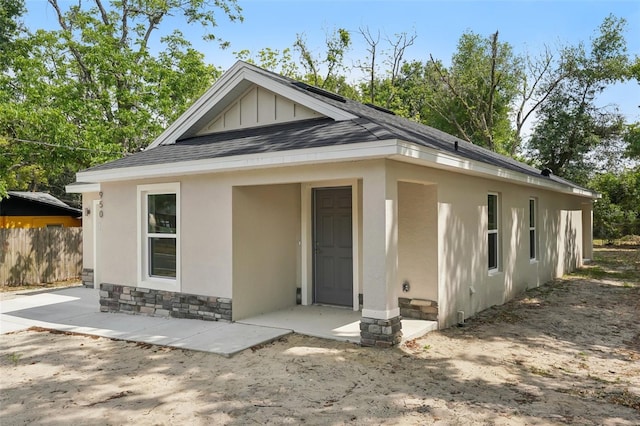 view of front of house with stone siding, fence, roof with shingles, and stucco siding