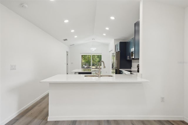 kitchen featuring a peninsula, light countertops, a sink, light wood finished floors, and vaulted ceiling
