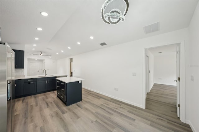 kitchen featuring light wood-style floors, dark cabinetry, light countertops, a peninsula, and visible vents