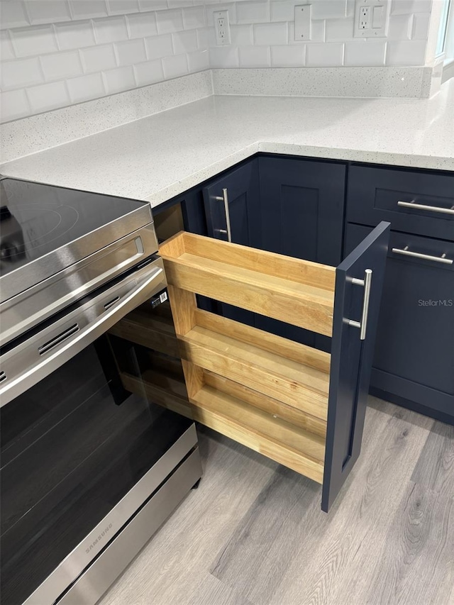 details featuring stainless steel electric range, light wood-style floors, decorative backsplash, and blue cabinets