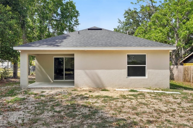 rear view of property with fence, a shingled roof, a patio area, and stucco siding