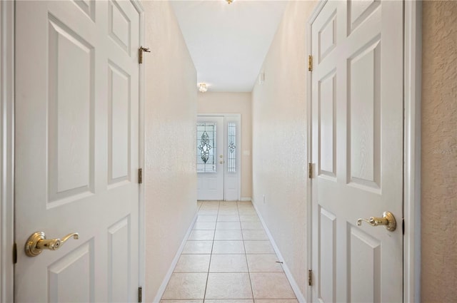 corridor featuring baseboards, a textured wall, and light tile patterned flooring