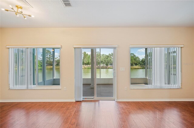 empty room featuring wood-type flooring, visible vents, baseboards, a water view, and a notable chandelier