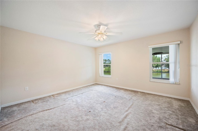 carpeted spare room featuring a ceiling fan, baseboards, and a wealth of natural light