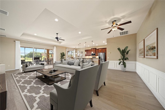 living room with a ceiling fan, visible vents, a tray ceiling, and light wood-style floors