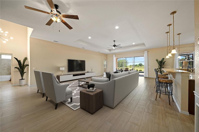 living area featuring ceiling fan, baseboards, light wood-style flooring, and a tray ceiling