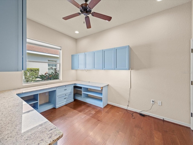 unfurnished office featuring baseboards, wood finished floors, ceiling fan, and built in desk