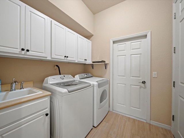 washroom featuring a sink, cabinet space, light wood-style floors, washing machine and dryer, and baseboards