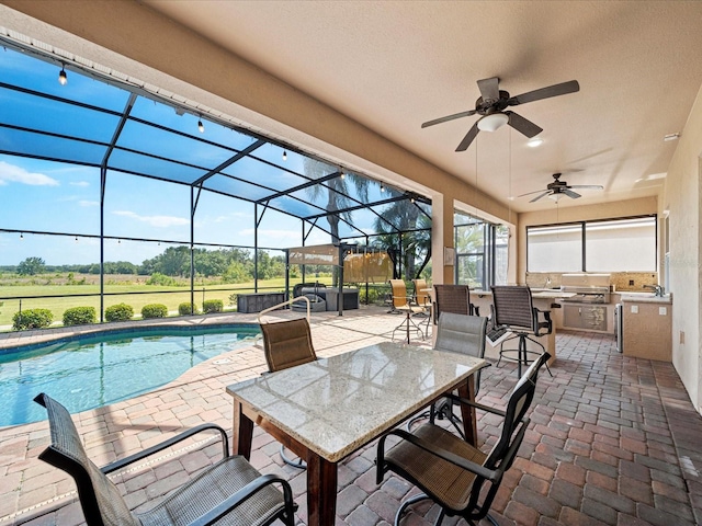 view of patio / terrace with a lanai, a ceiling fan, an outdoor pool, and exterior kitchen