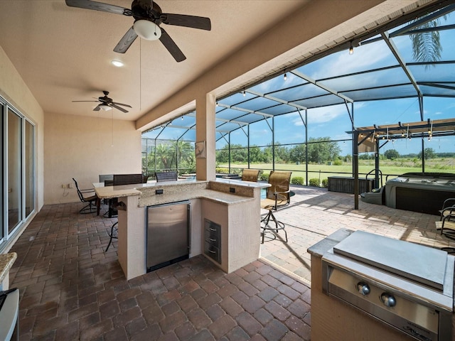 view of patio with outdoor dry bar, a ceiling fan, glass enclosure, and a hot tub