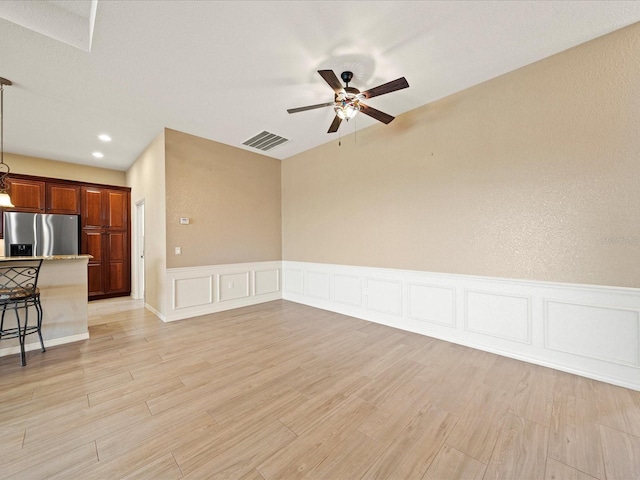 unfurnished living room featuring visible vents, ceiling fan, a decorative wall, and light wood-style floors