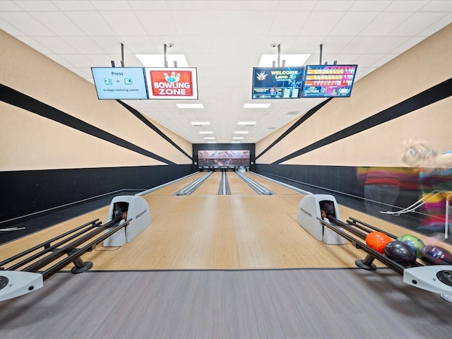 recreation room with a bowling alley, a paneled ceiling, and wood finished floors