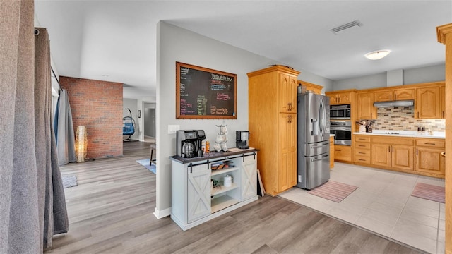 kitchen featuring visible vents, decorative backsplash, under cabinet range hood, light wood finished floors, and appliances with stainless steel finishes