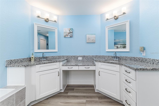 full bathroom with a bath, vanity, and wood finished floors