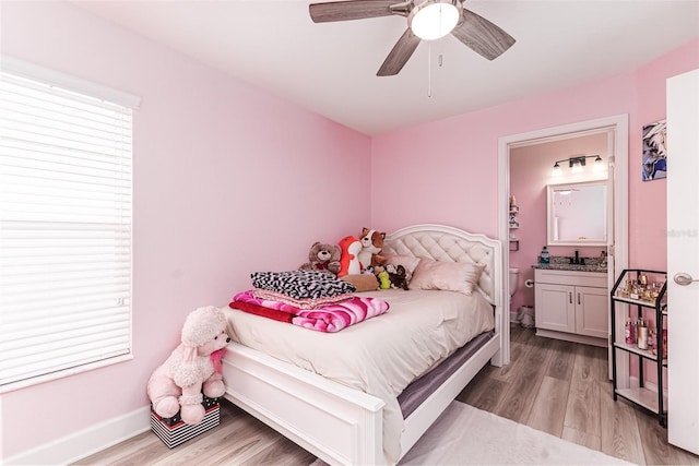 bedroom featuring light wood-style floors, baseboards, ensuite bathroom, and a sink