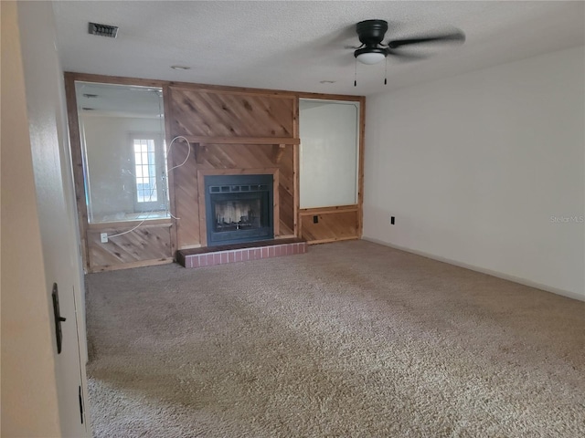 unfurnished living room with visible vents, a fireplace with raised hearth, carpet, and a ceiling fan