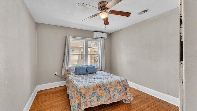 bedroom featuring baseboards, visible vents, wood finished floors, and a wall mounted air conditioner