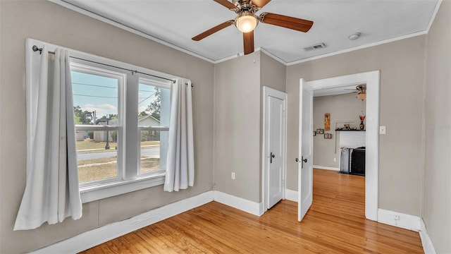 unfurnished room with a ceiling fan, visible vents, baseboards, light wood finished floors, and ornamental molding