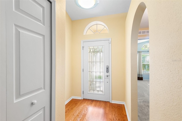 doorway with visible vents, arched walkways, wood finished floors, baseboards, and a textured wall